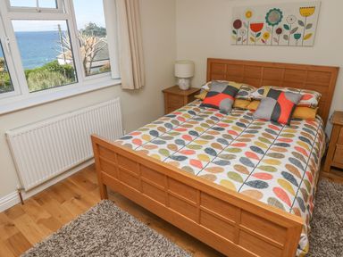 A bedroom with a wooden bed and colorful bedding near a window overlooking the sea at Hagar Vor in Marazion
