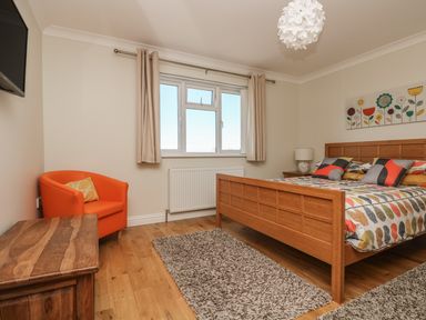A bedroom with a wooden bed with colorful bedding an orange chair a wooden chest a window and a wall painting at Hagar Vor in Marazion