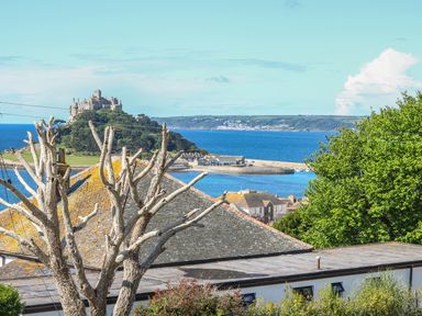 A coastal view with a castle on a hill surrounded by water and rooftops of houses in the foreground at Hagar Vor in Marazion
