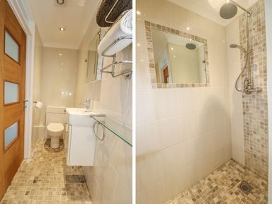 A bathroom with a toilet, sink, towel racks, and a tiled walk-in shower with mirror at Hagar Vor in Marazion