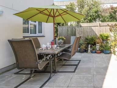 An outdoor patio with a table and chairs under a green umbrella and potted plants along a wooden fence at Hagar Vor in Marazion