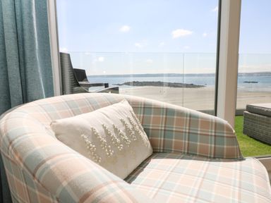 A plaid upholstered armchair with a decorative white pillow next to a glass window overlooking a beach and ocean at Higher Mount View in Marazion