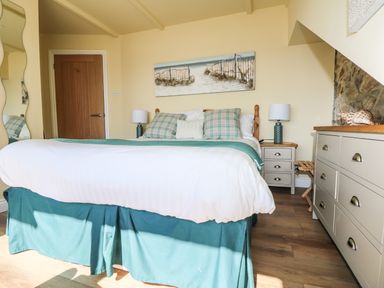 A bedroom with a bed two bedside tables lamps a dresser and a painting at Higher Mount View in Marazion
