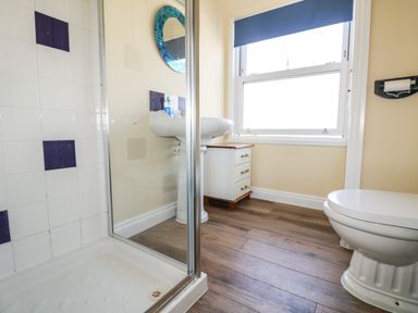A bathroom with a shower enclosure a white toilet a sink with a mirror above and a window with a blue blind at Higher Mount View in Marazion