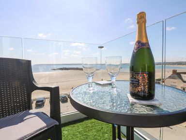 A balcony with a glass table holding a champagne bottle and two glasses overlooking a beach at Higher Mount View in Marazion