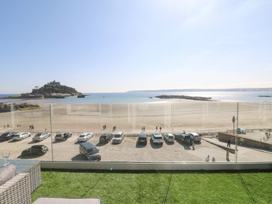 A balcony with glass railing overlooking a beach parking lot and an island with a castle at Higher Mount View in Marazion