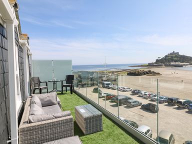 A balcony with wicker furniture overlooking a beach and castle at Higher Mount View in Marazion