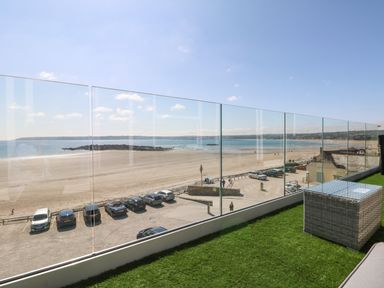 A balcony with glass railing overlooking a beach and parked cars at Higher Mount View in Marazion