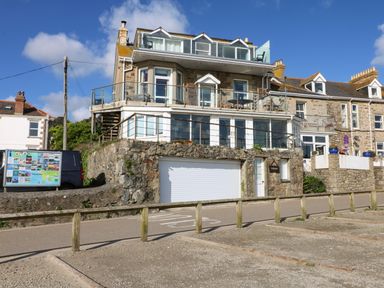 A multi-story stone house with balconies and glass railings by a road with parking spaces at Higher Mount View in Marazion