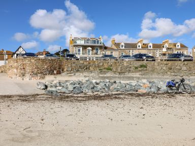 A bicycle parked on a sandy beach with rocks and stone wall with cars and houses in the background at Higher Mount View in Marazion