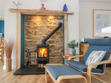 A room with a stone fireplace and wood burning stove next to a blue chair and ottoman with a patterned cushion at Higher Mount View in Marazion