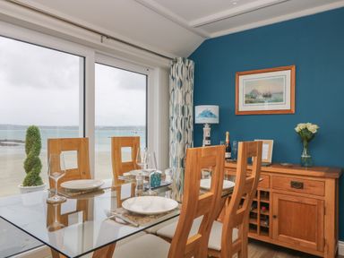 A dining room with wooden chairs and a glass table next to large windows with a sea view at Higher Mount View in Marazion