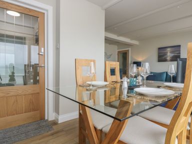 A dining area with a glass table and wooden chairs set with plates and wine glasses at Higher Mount View in Marazion