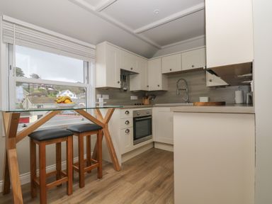A kitchen with wooden stools glass table and cream cabinets at Higher Mount View in Marazion