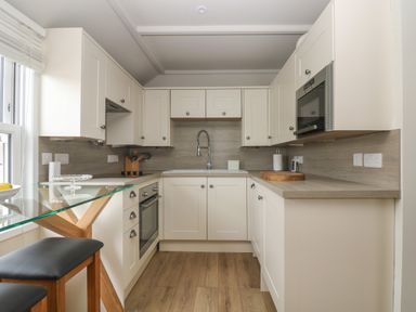A kitchen with white cabinets wooden floor glass countertop and stools at Higher Mount View in Marazion
