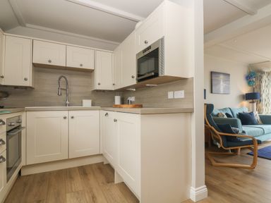 A kitchen with white cabinets sink and oven next to a living room with blue sofa and chair at Higher Mount View in Marazion