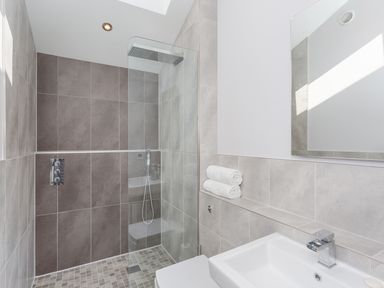 A bathroom with a walk-in shower a tiled wall and floor a sink with a faucet and two rolled towels on a shelf at Lake View in Kingsand and Cawsand