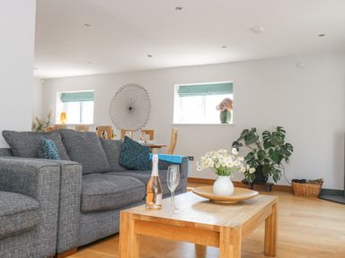 A living room with a gray sofa wooden coffee table with flowers and a bottle at Lake View in Kingsand and Cawsand