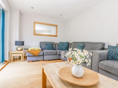 A living room with a grey sectional sofa cushions a white vase with flowers on a wooden coffee table and a wooden framed mirror on the wall at Lake View in Kingsand and Cawsand