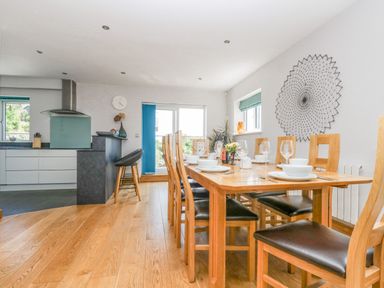 A dining area with a wooden table set with plates and glasses next to a kitchen with white cabinets at Lake View in Kingsand and Cawsand