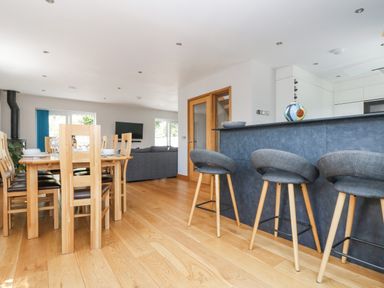 A dining area with a wooden table and chairs next to a kitchen counter with bar stools and a living room with a sofa at Lake View in Kingsand and Cawsand