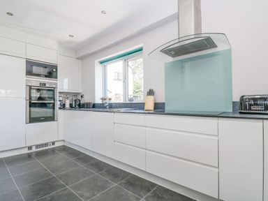 A modern kitchen with white cabinets black countertop gray tiled floor built-in oven microwave electric hob glass extractor fan knife block toaster and window at Lake View in Kingsand and Cawsand
