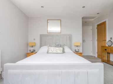A bedroom with a white bed and headboard between two wooden bedside tables with lamps a wooden door and table with a vase in Lake View Kingsand and Cawsand