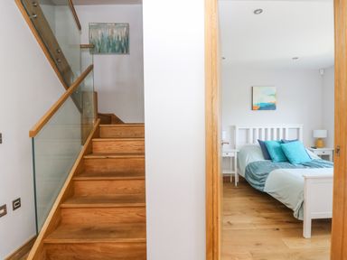 Wooden staircase with glass railing next to a bedroom with a white bed and blue pillows at Lake View in Kingsand and Cawsand
