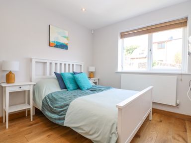 A bedroom with a white bed frame two side tables with lamps and a window at Lake View in Kingsand and Cawsand
