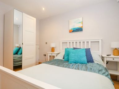 A bedroom with a white bed frame blue and turquoise pillows bedside tables with orange lamps and a wardrobe with a mirrored door at Lake View in Kingsand and Cawsand