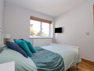 A bedroom with a bed with teal and blue pillows a window with blinds and a wall-mounted TV at Lake View in Kingsand and Cawsand