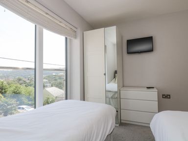 A bedroom with two beds a wardrobe with mirrored door a chest of drawers and a wall-mounted television at Lake View in Kingsand and Cawsand
