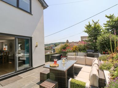 An outdoor patio with wicker furniture a glass table and garden plants at Lake View in Kingsand and Cawsand