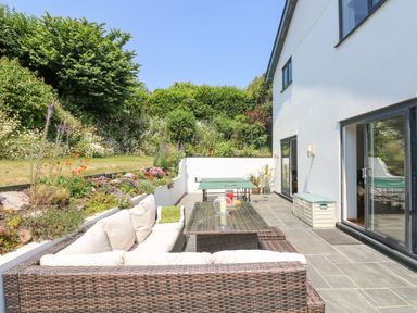 An outdoor patio with a wicker sofa set table and ping pong table next to a white house at Lake View in Kingsand and Cawsand
