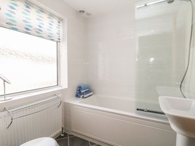 A bathroom with a bathtub shower combination blue towels window with fish patterned blind and white sink at Gwillen in Mawgan Porth