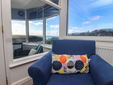 A blue armchair with a patterned cushion next to windows showing an outdoor view at Gwillen in Mawgan Porth