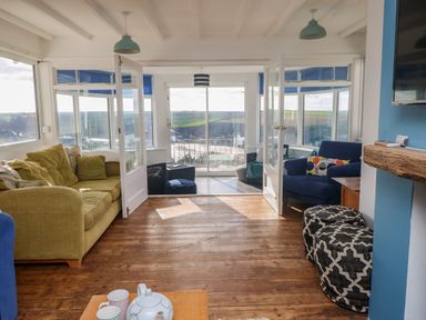 A living room with two sofas poufs a wooden floor and a tea set on a table at Gwillen in Mawgan Porth