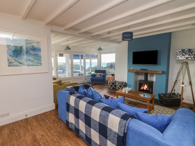 A living room with blue sofas a fireplace wall mounted tv and ocean view at Gwillen in Mawgan Porth