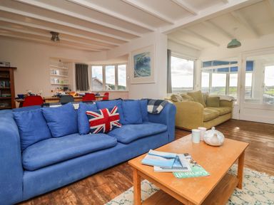 A living room with blue and beige sofas a wooden coffee table and a dining area in the background at Gwillen in Mawgan Porth