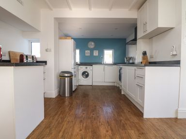 A kitchen with white cabinets a washing machine a refrigerator a toaster and a trash can at Gwillen in Mawgan Porth