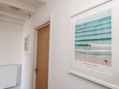 A hallway with white walls wooden door radiator and framed surf poster at Gwillen in Mawgan Porth
