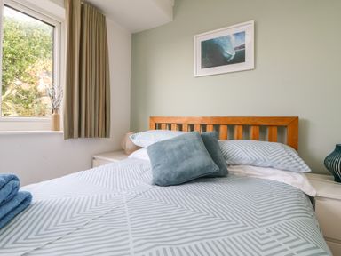 A bedroom with a bed with blue patterned bedding and pillows next to a window with striped curtains at Gwillen in Mawgan Porth
