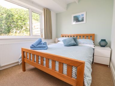 A bedroom with a wooden bed frame blue bedding bedside tables and a window at Gwillen in Mawgan Porth