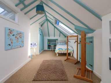 A bedroom with a single bed a skylight window a world map on the wall and wooden clothes racks at Gwillen in Mawgan Porth