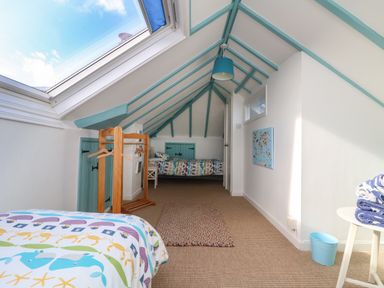 A bedroom with slanted ceiling beams and two beds with patterned bedding at Gwillen in Mawgan Porth