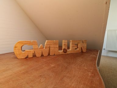 A wooden block word sculpture on a wooden table in a room with a radiator at Gwillen in Mawgan Porth