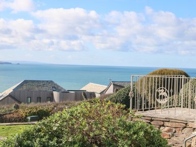 A coastal view with houses and a metal railing overlooking the sea at Gwillen in Mawgan Porth