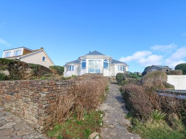 A path leading to a house with stone walls and bushes on either side at Gwillen in Mawgan Porth