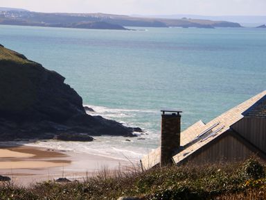 A coastal view with a rocky cliff beach chimney and roof visible at Gwillen in Mawgan Porth