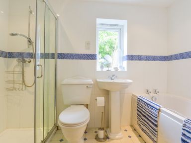 A bathroom with a shower cubicle toilet pedestal sink and bathtub with striped towels at Goslings Bradford Holsworthy